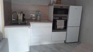 Eine kompakte Küche mit Spüle, Herd und Kühlschrank. An der Wand hängen drei gerahmte Bilder und auf der Arbeitsfläche steht ein Blumentopf.