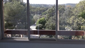 Ein Zimmer mit großem Fenster und Blick auf ein bewaldetes Gebiet sowie eine Straße.