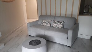 Ein modernes Wohnzimmer mit einem grauen Sofa, zwei gemusterten Kissen und einem weißen Couchtisch mit geometrischem Design.