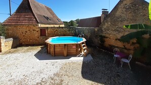 Une maison en pierre avec une piscine en bois, une grange à toit rouge et un mur en pierre.