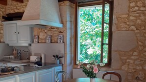 Une cuisine rustique avec un mur en pierre, un plafond en bois, des armoires blanches et une table à manger avec des chaises.