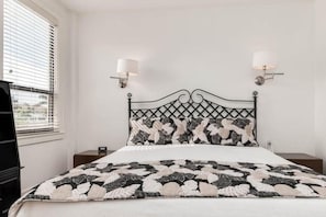 A bed with a patterned headboard, two bedside lamps, and a window with blinds.