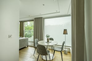 A modern room with a round table, grey chairs, a sofa, and a large window with curtains.