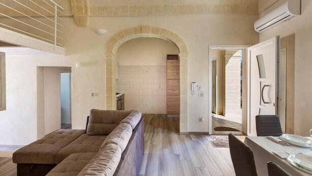 Un salon moderne avec un canapé d’angle, un coin repas comprenant une table et des chaises, et une porte en arc donnant sur une autre pièce.