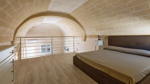 Une chambre avec un plancher en bois, un lit avec une tête de lit, une table de chevet et une fenêtre donnant sur l’extérieur.