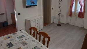 Et spiseområde med et bord dækket til to personer, et tv ophængt på væggen og en dør, der fører til et andet rum.