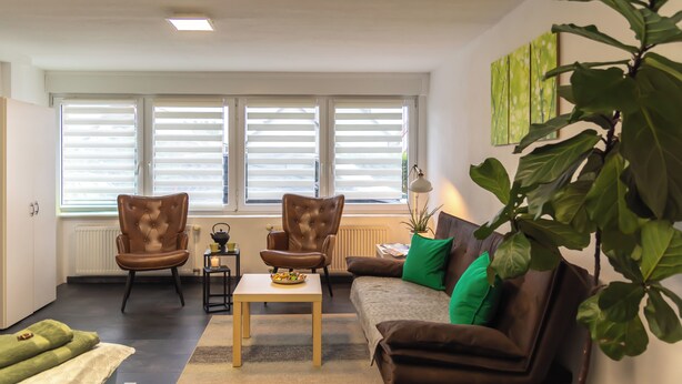 A living room with a sofa, two armchairs, a coffee table, and a large window with blinds.