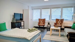 A room with a bed, a desk, two chairs, a television, and a window with blinds.