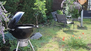 A backyard with a black grill, a chair, and a wooden fence.