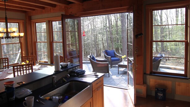 A wooden cabin with a kitchen, dining area, and a patio with outdoor seating. - Stille Wasser, Quiet, secluded spot on Saco River with Dock (Boat lift option) (Buxton)