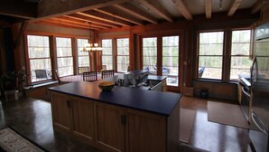 A spacious kitchen with wooden cabinets, a large island, and a view of the outdoors through large windows. - Stille Wasser, Quiet, secluded spot on Saco River with Dock (Boat lift option) (Buxton)