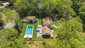 An aerial view of a residential property with a swimming pool, a patio with outdoor furniture, and a large house with a sloped roof. - Traditional-style home with pops of patterns and vibrant colors, private... (Sag Harbor)