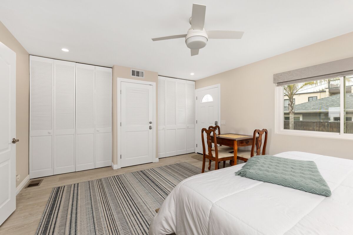 A bedroom with a bed, a desk, and a chair. There are closets and a window.