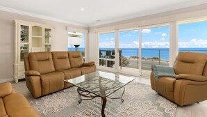 A spacious living room with a glass coffee table, two brown leather sofas, and a large window offering a view of the ocean. - BEACH FACING! Large 3BR - 180 panoramic ocean views, steps to sand and Village! (Carlsbad)