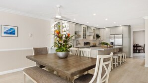 A modern kitchen with white cabinets, a large island, and a dining area with a wooden table and chairs. - BEACH FACING! Large 3BR - 180 panoramic ocean views, steps to sand and Village! (Carlsbad)