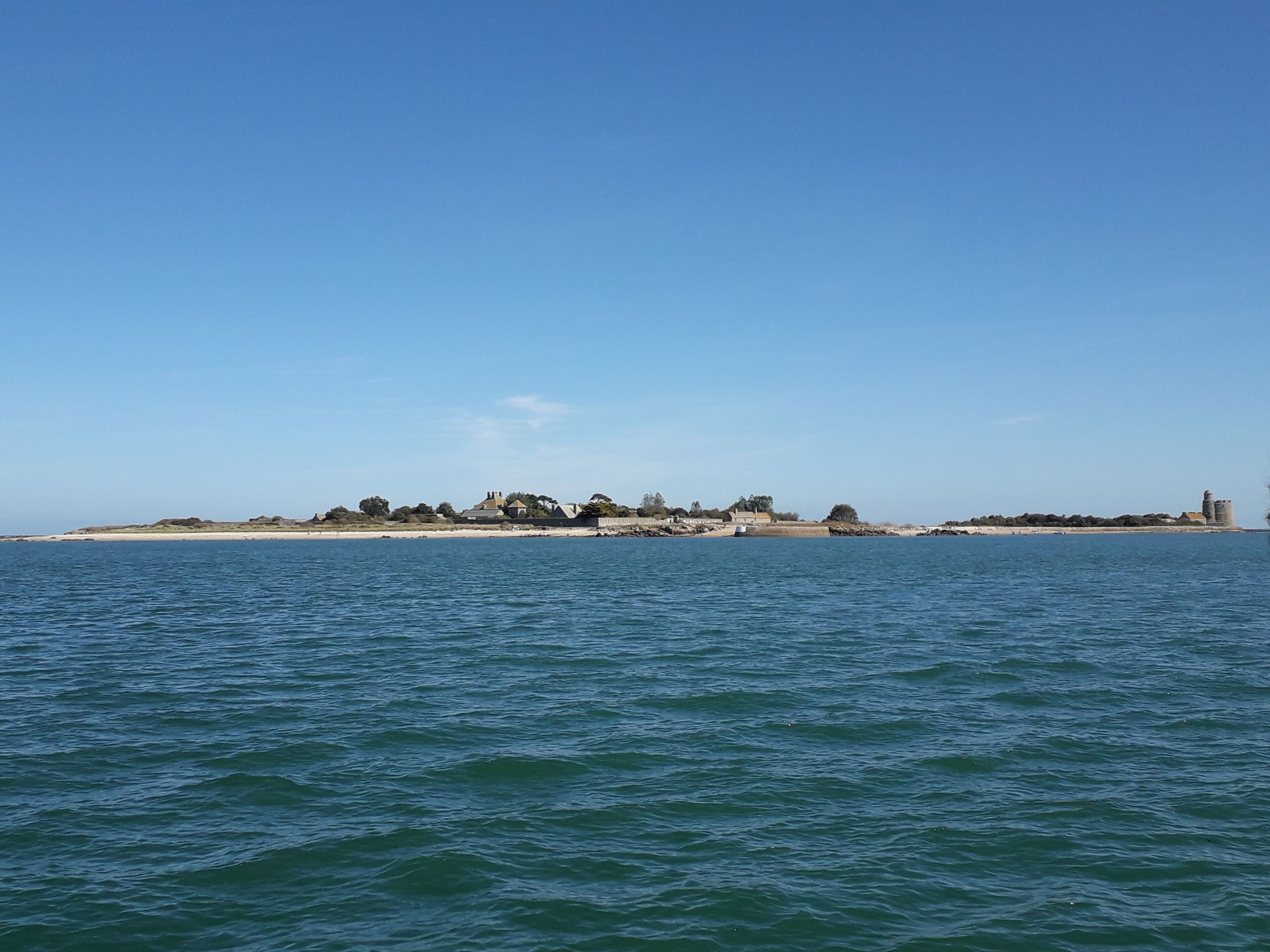 Une vue sur la côte, avec une plage de sable et un petit village composé de bâtiments et d’un phare.