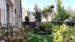 A garden with a stone wall, a palm tree, and various shrubs. - Fully renovated cottage with swimming pool in the heart of Cotentin (MONTEBOURG)