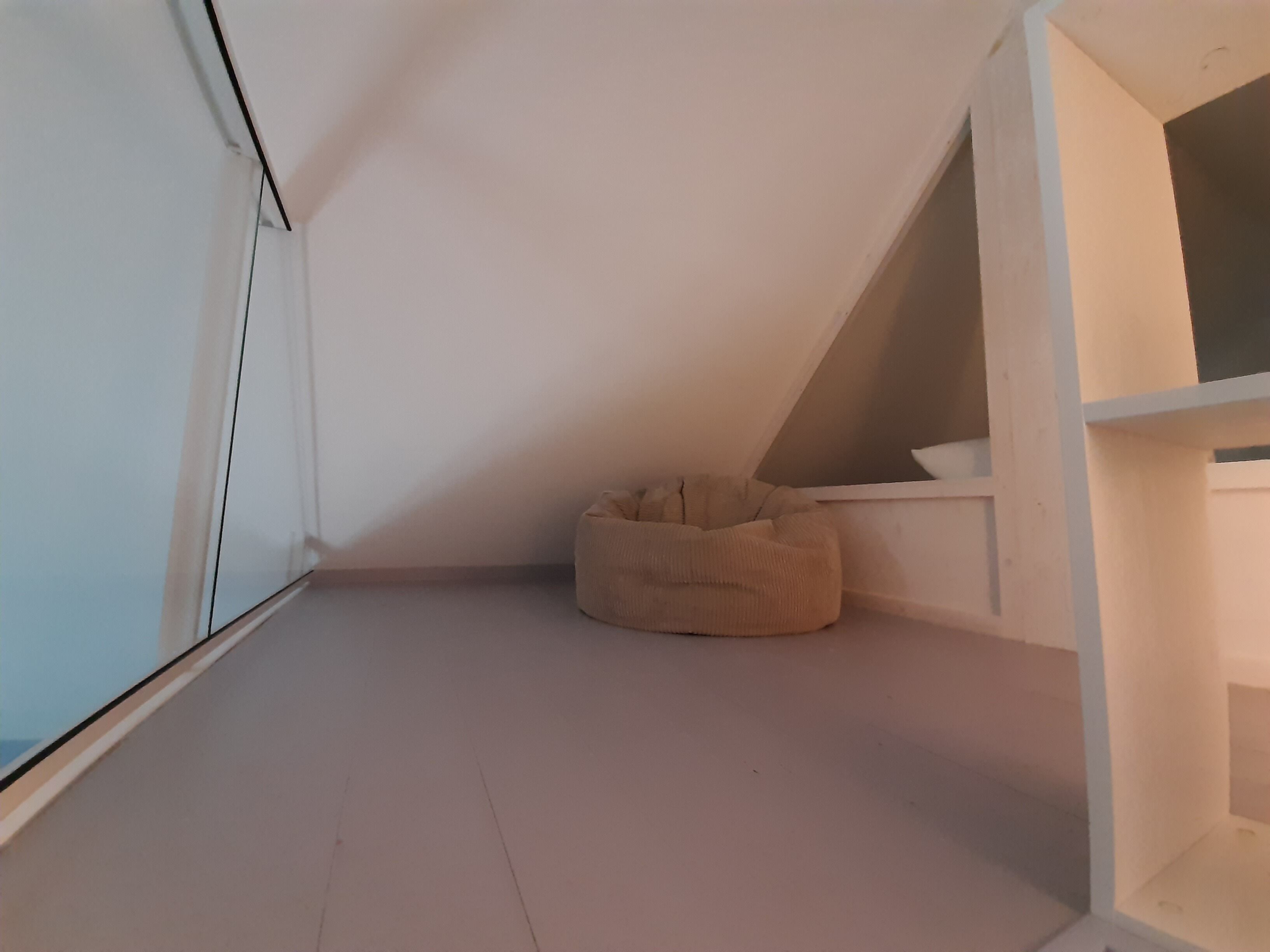 A room with a sloped ceiling, a white floor, and a beige bean bag chair.