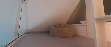 A room with a sloped ceiling, a white floor, and a beige bean bag chair.