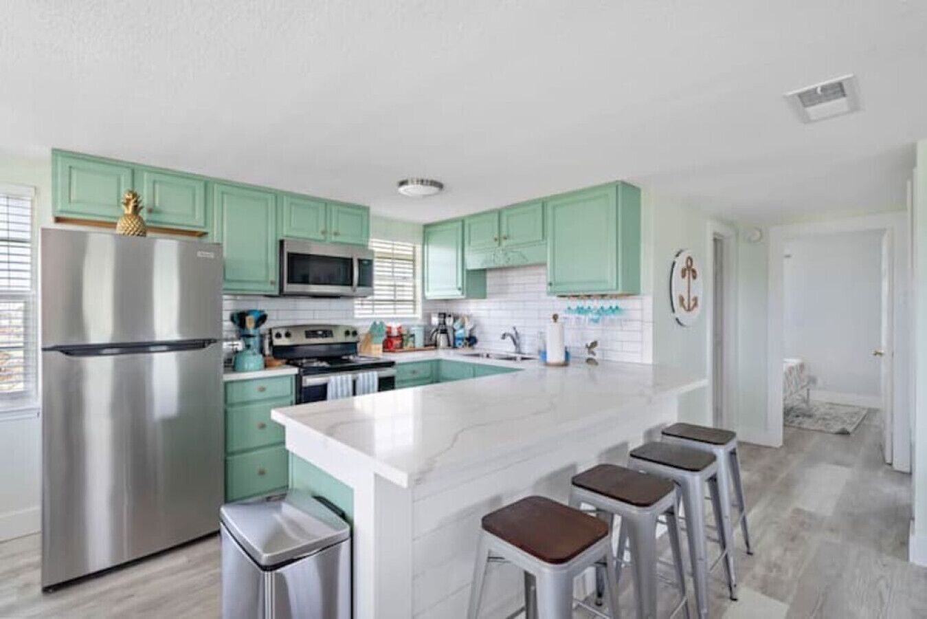 A modern kitchen with teal cabinets, stainless steel appliances, and a large island with bar stools.
