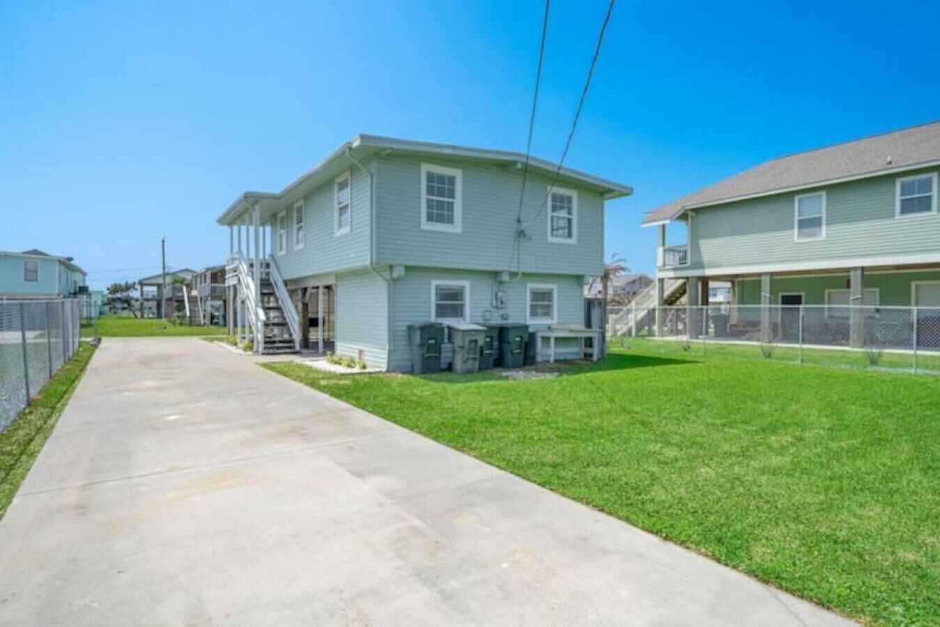 A residential area with a two-story house featuring a front porch, a visible staircase, and a fenced yard.