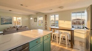 A kitchen with a large island, a dining area with stools, and a view of the outside. - Cozy Cottage with Game Room, Close to Beach (Galveston)