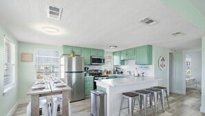 A modern kitchen with a central island, stainless steel appliances, and light green cabinetry. - Cozy Cottage with Game Room, Close to Beach (Galveston)