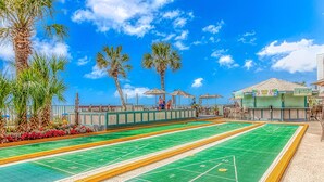 A craps table with a green felt surface, surrounded by a low concrete barrier, palm trees, and outdoor seating with umbrellas. - BEAUTIFUL PRIVATE 9TH FLOOR OCEAN VIEW CONDO; NEWLY RENOVATED OCEANFRONT RESORT (Myrtle Beach)