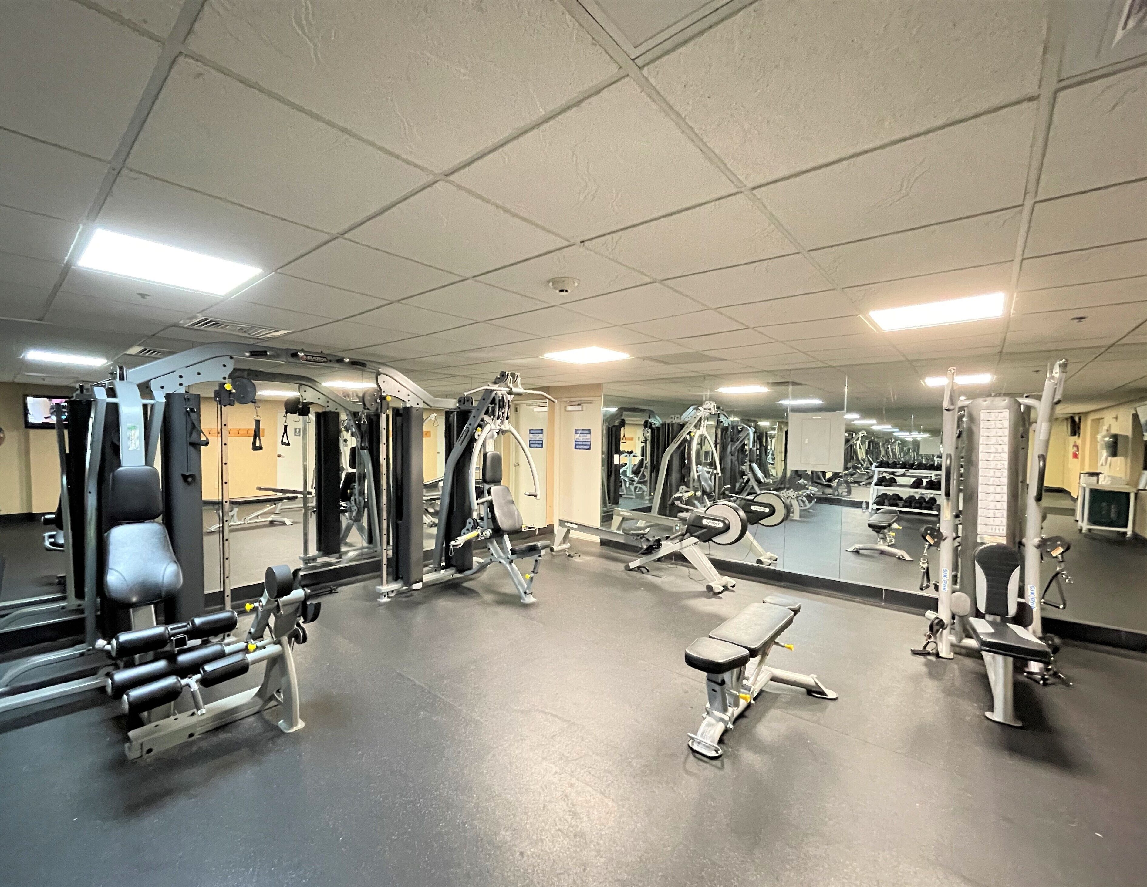 Une salle de sport équipée de divers appareils d’exercice, dotée d’un grand miroir et d’un téléviseur fixé au mur.