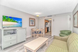 A compact living space with a television, dining table, chairs, a sofa, and a kitchen area.