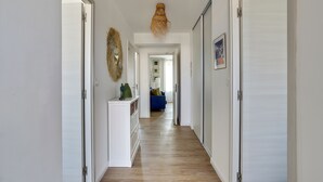 Ein Flur mit weißen Wänden und Holzboden, der zu einem Raum mit einem blauen Sofa und einem Zier-Spiegel führt.