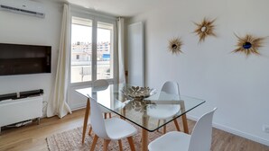 Ein modernes Wohnzimmer mit einem Glastisch, weißen Stühlen, einem Flachbildfernseher und Wandbildern.