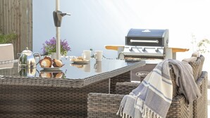 Ein Essbereich im Freien mit Grill, Korbmöbeln und einem Tisch mit Speisen und Getränken.