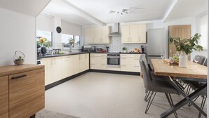 Eine moderne Küche mit hellen Schränken, einer zentralen Kochinsel und einem Essbereich mit einem Holztisch und Stühlen.