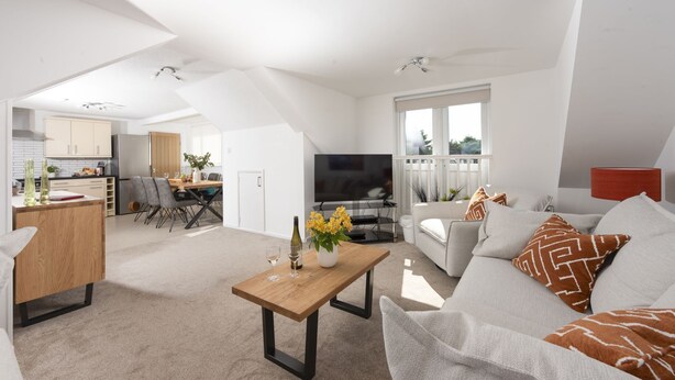 Ein großzügiger Wohnbereich mit Couchtisch aus Holz, einer Couch mit gemusterten Kissen, einem Fernseher und einem Essbereich mit Holztisch und Stühlen.