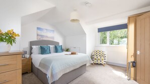 Ein Schlafzimmer mit Bett, Nachttisch, Kommode, einem Fenster mit Blick und einer Tür.