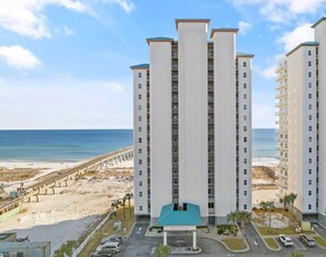 A high-rise hotel with a beach view, multiple balconies, and a parking area.