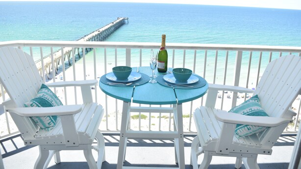 A balcony with two white chairs and a table, overlooking a pier and the sea. - Best view on the Gulf! Heated pool and beach gear included! Book today!  (Navarre)