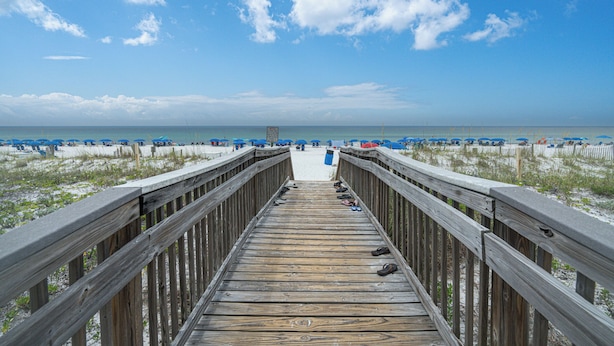 Une promenade en bois menant à une plage parsemée de parasols et de sable.