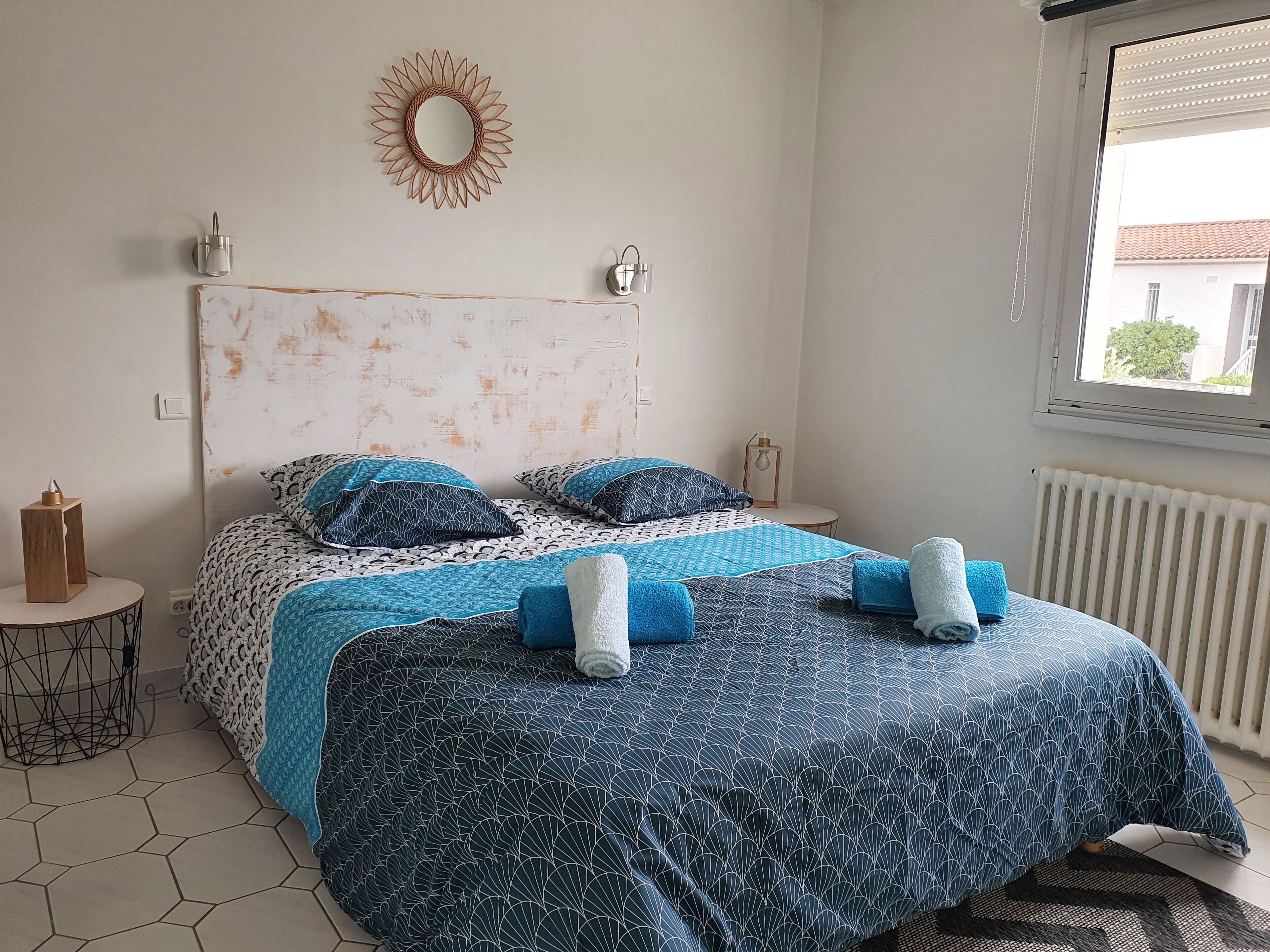 Une chambre à coucher avec un lit, un miroir rond, une petite table et un radiateur.