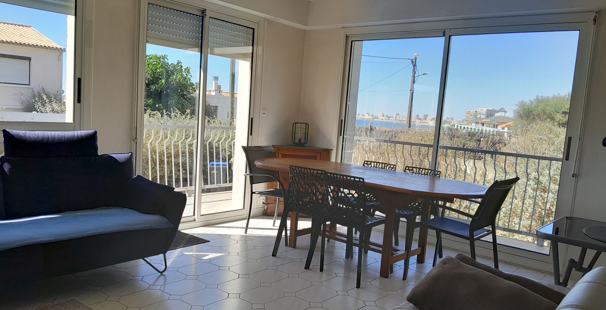 Un salon moderne avec un canapé, une table à manger et des chaises, et une vue sur le paysage urbain à travers de grandes fenêtres.