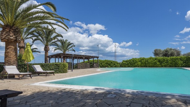 A clear blue swimming pool with lounge chairs and a pergola, surrounded by palm trees and a hedge. - Junior Suite Deluxe - Hotel Lady Lusya ★★★★ (Sicilia)