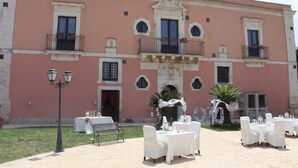 A building with a pink facade, multiple balconies, and outdoor seating areas with white tables and chairs. - Junior Suite Deluxe - Hotel Lady Lusya ★★★★ (Sicilia)