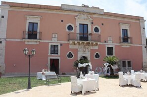 Un edificio con fachada rosa, varios balcones y terrazas al aire libre con mesas y sillas blancas.