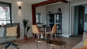 A modern living room with a dining area, wooden floors, and a kitchen in the background. - Apartment with lake view (Waldeck)