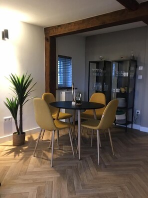 A dining area with a round table and four chairs, a potted plant, and a glass cabinet with dishes.