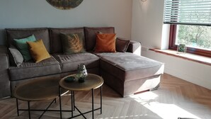 A modern living room with a sectional sofa, a small round table, and a large wall painting. - Apartment with lake view (Waldeck)