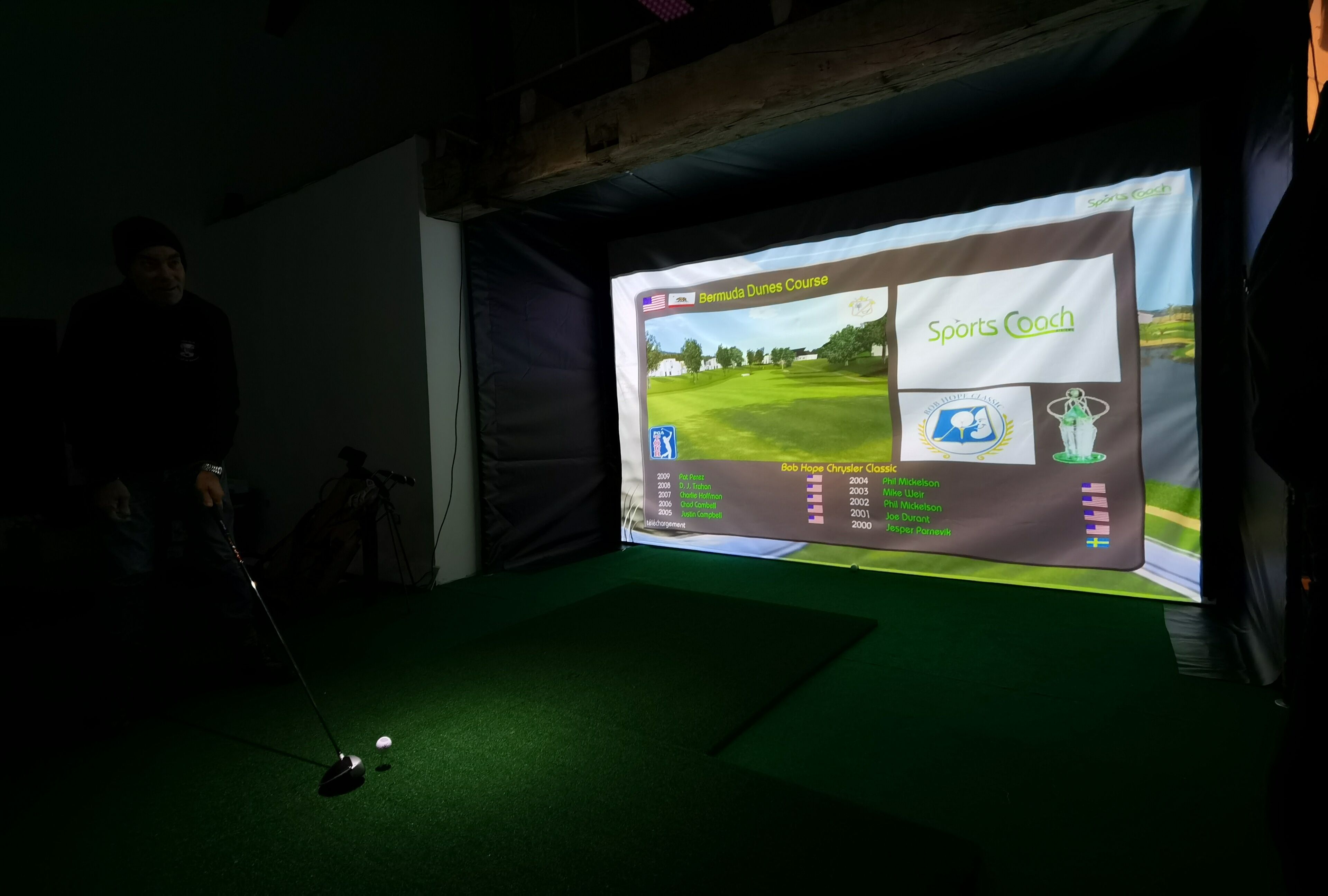 Configuración de simulador de golf con una pantalla mostrando un campo de golf y un club de golf sobre una alfombra.