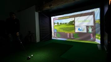 Configuración de simulador de golf con una pantalla mostrando un campo de golf y un club de golf sobre una alfombra.