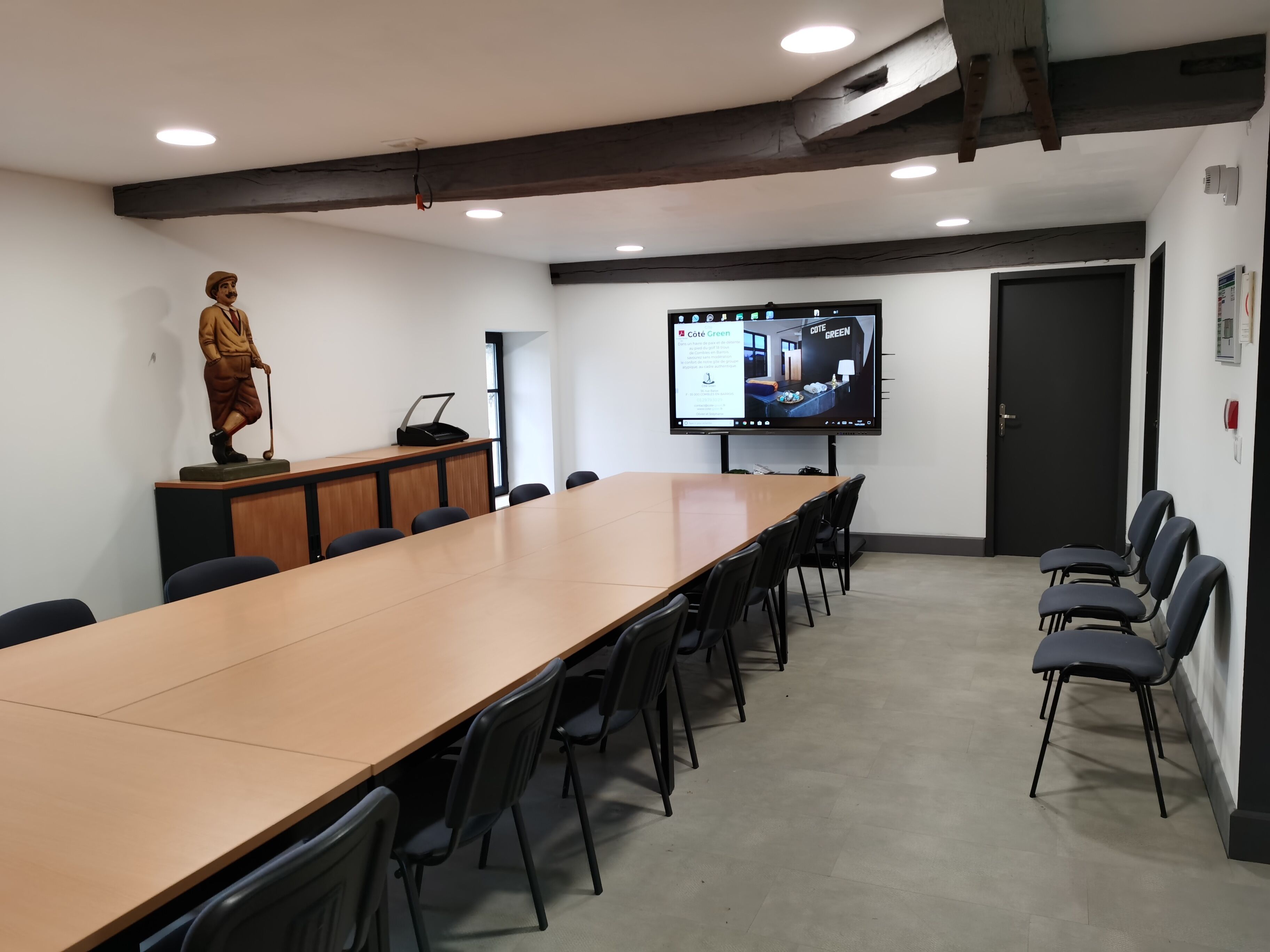 Une salle de conférence avec une longue table, des chaises, une statue, un écran de projection et une porte.